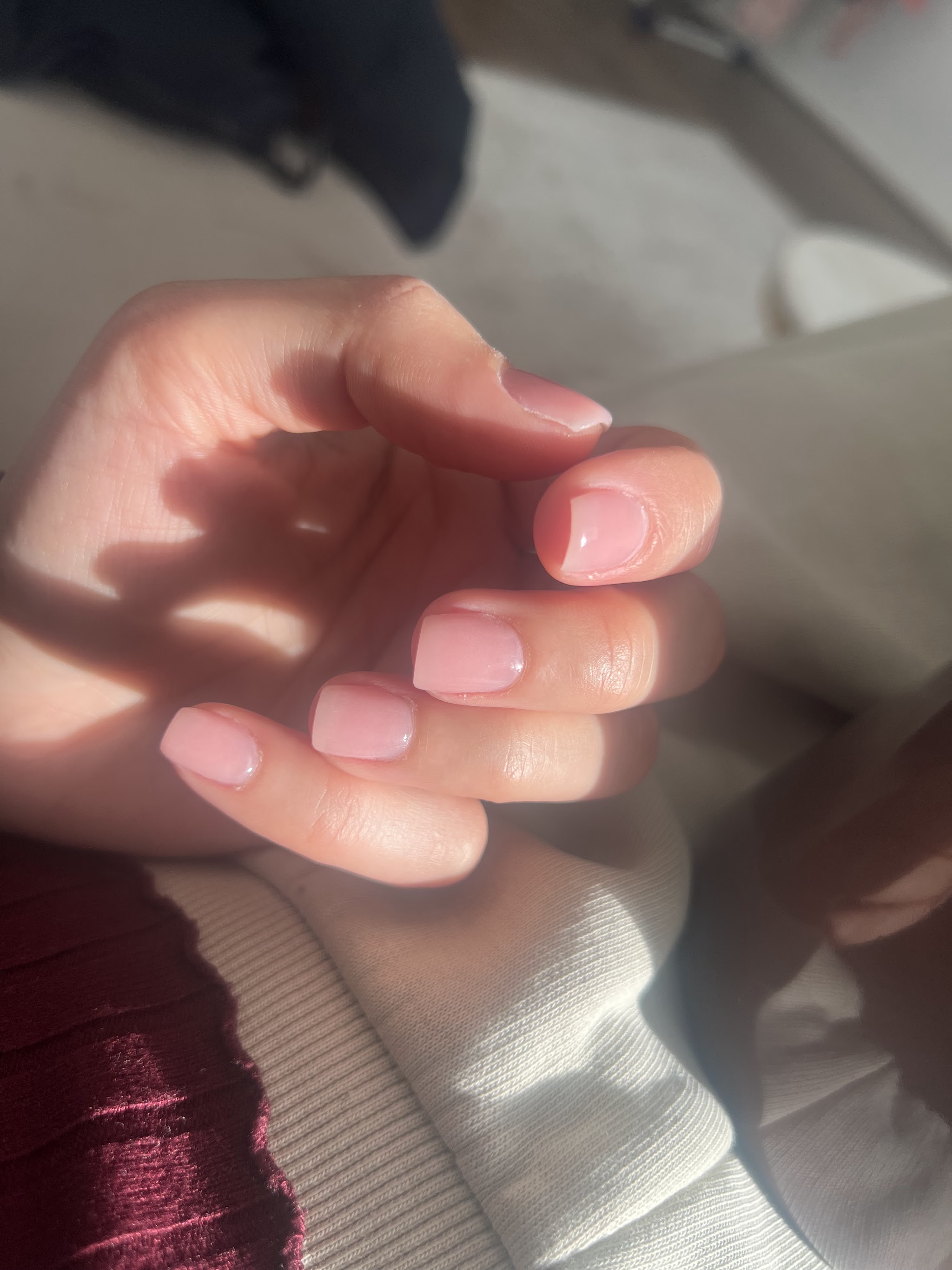 Korte natuurlijke nagels in zacht roze, in het zonlicht