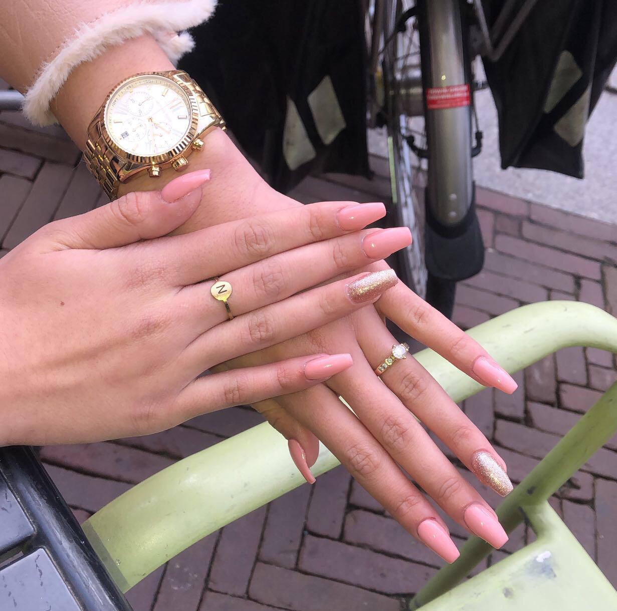 Twee handen met lange zachtroze nagels, één nagel met glitter