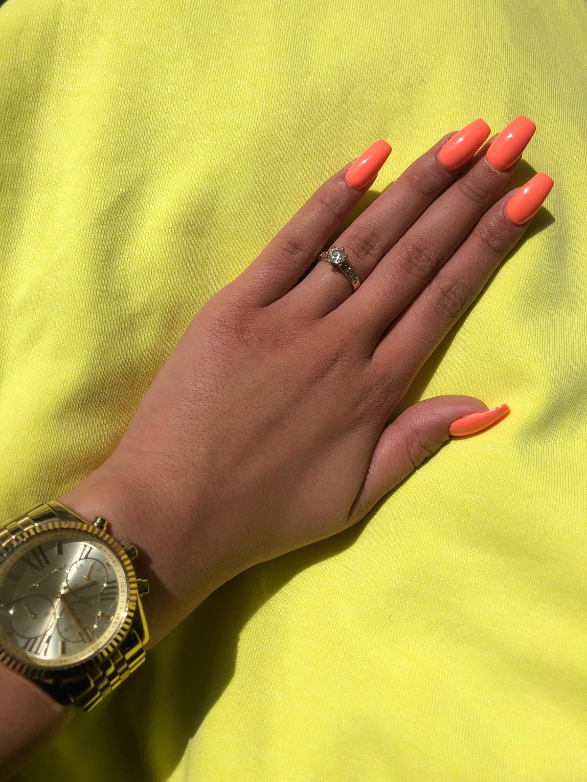 Hand met fel oranje nagels op een geel shirt